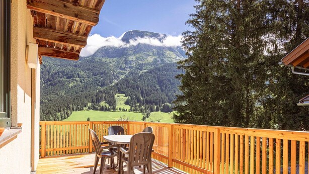 A wooden deck with a table and chairs overlooking a mountainous landscape.