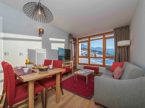 A modern living room with a dining area, a flat-screen TV, and large windows with a mountain view.