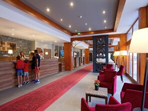 A hotel lobby with a reception desk, a red carpet, and red chairs.
