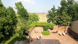 A patio area with brick flooring, a small garden with a hedge, and a view of a field.