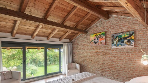 A bedroom with a large bed, a sofa, and a view through a sliding glass door.