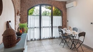A dining area with a brick wall, a large window with curtains, a table set for four, and a wicker basket on a counter.