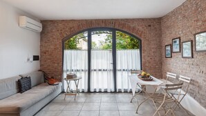 A cozy room with a brick wall, a sofa, a dining table with chairs, and a large window with curtains.