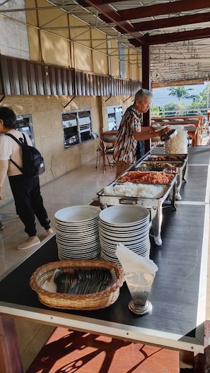 A buffet setup with food stations, stacked plates, and a person serving food. - Hotel Nirwana Batu (Batu)