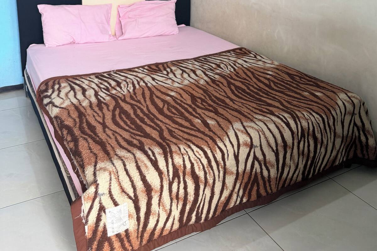 A bedroom with a bed, a headboard, a wall painting, and a tiled floor.