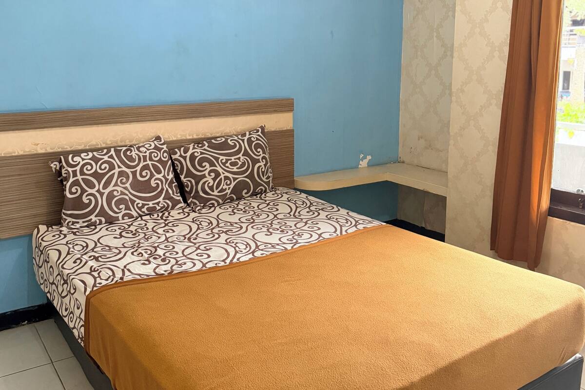 A bed with patterned bedding, a headboard, and a window with curtains.