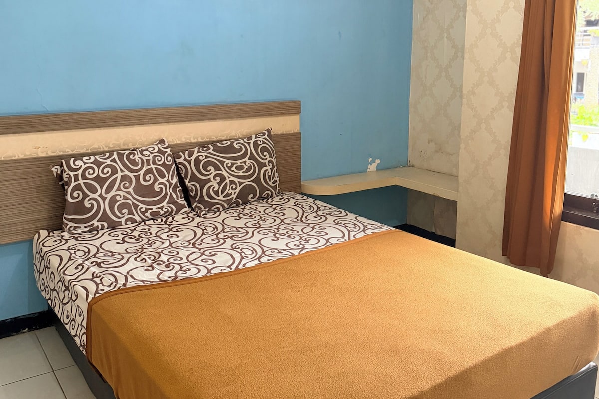 A bed with patterned bedding, a headboard, and a window with curtains.