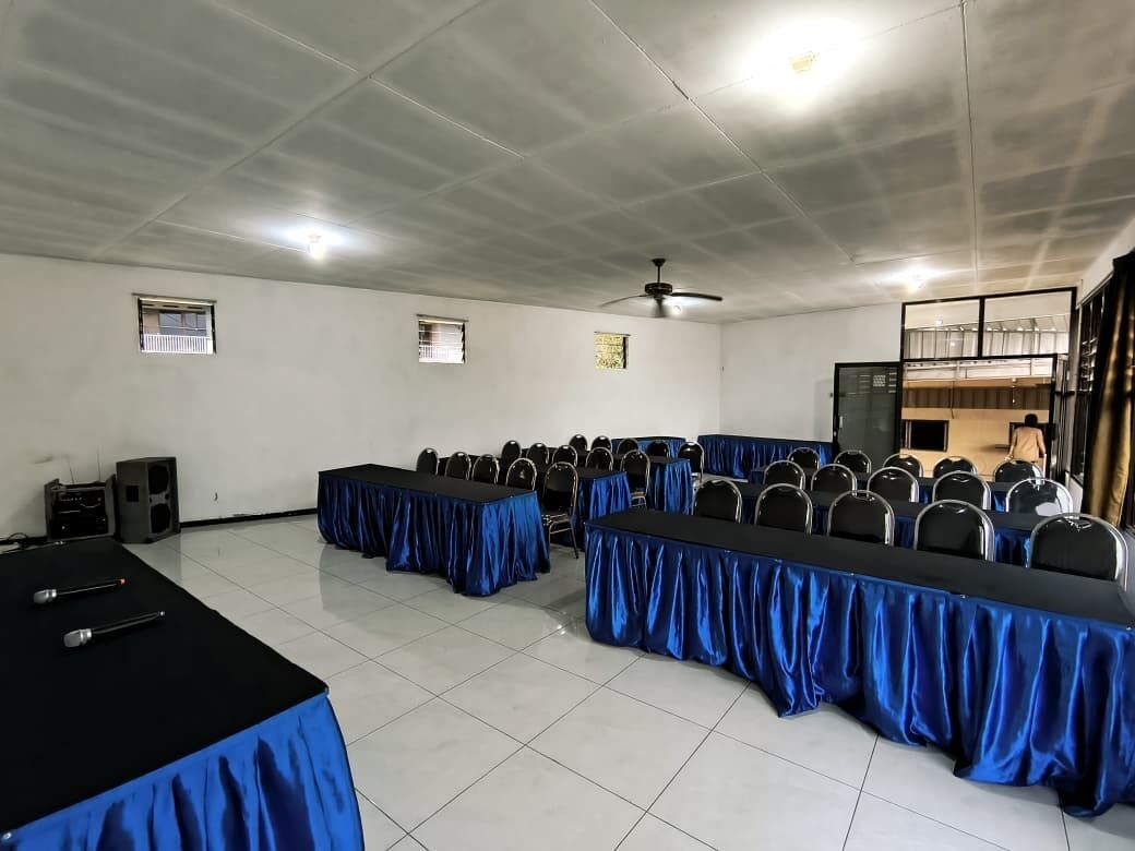 A conference room with rows of tables, chairs, a ceiling fan, and a speaker.