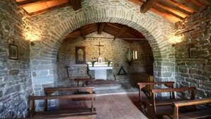 Un intérieur aux murs de pierre, avec des bancs en bois, un autel central et une croix.