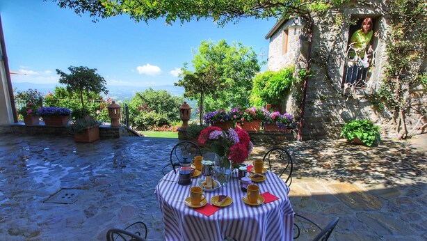 Un espace de restauration en plein air avec une table dressée pour deux personnes, entouré de murs en pierre et de plantes en pot.