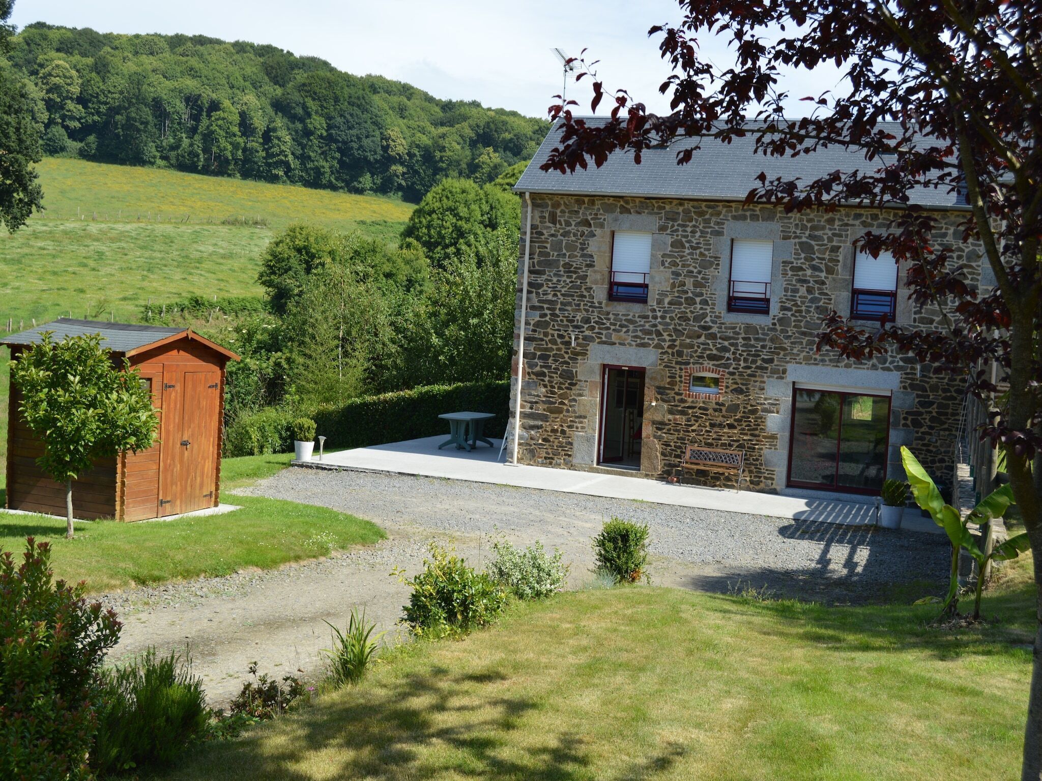 Une maison en pierre avec un petit jardin, un abri en bois et une vue sur une colline verdoyante.