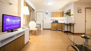Una habitación de hotel moderna con televisión, zona de comedor, cocina y mesa de vidrio.