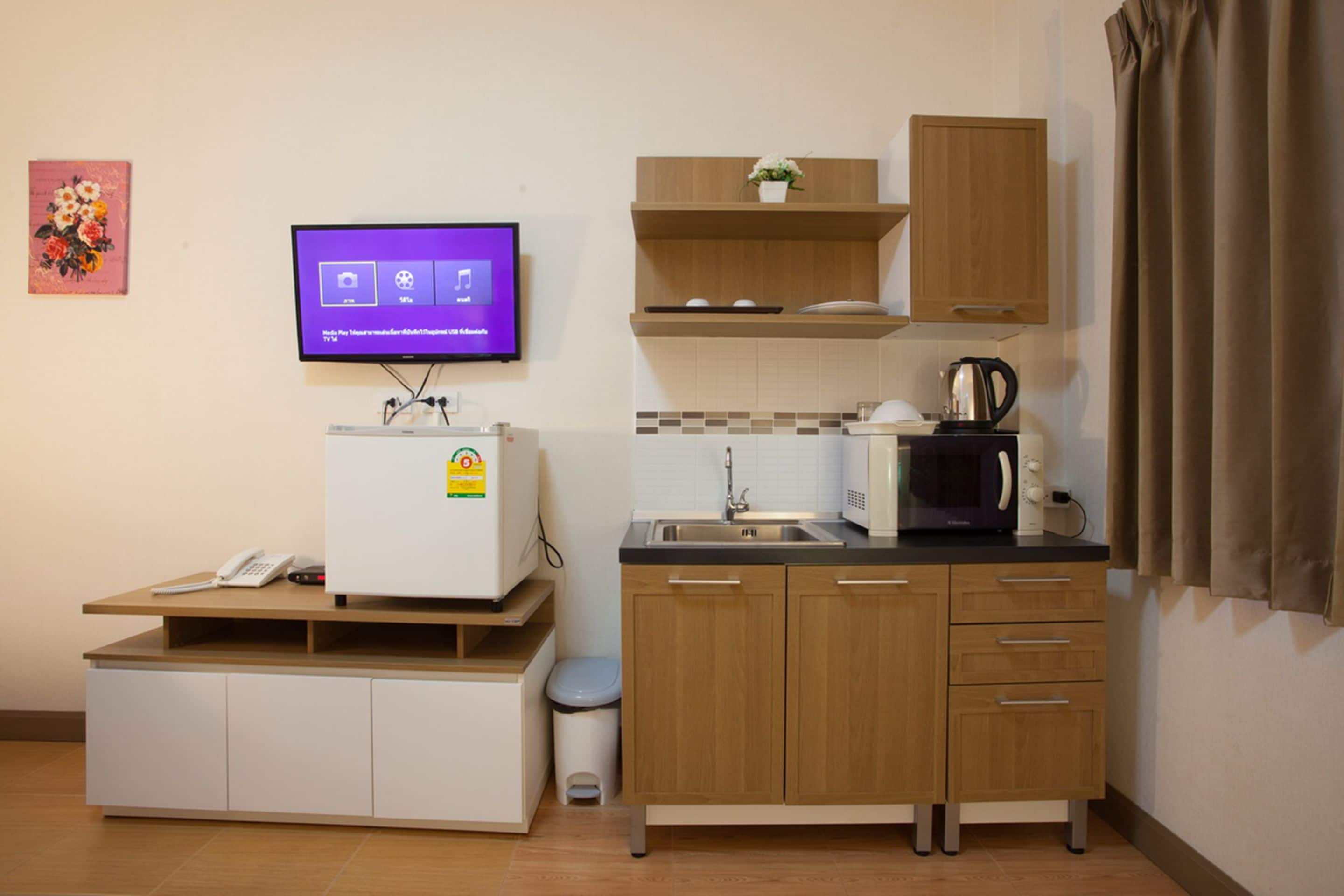 Une petite cuisine équipée d’un four à micro-ondes, d’une machine à café et d’un petit réfrigérateur. Un téléviseur est fixé au mur, et une poubelle se trouve à côté de l’évier.