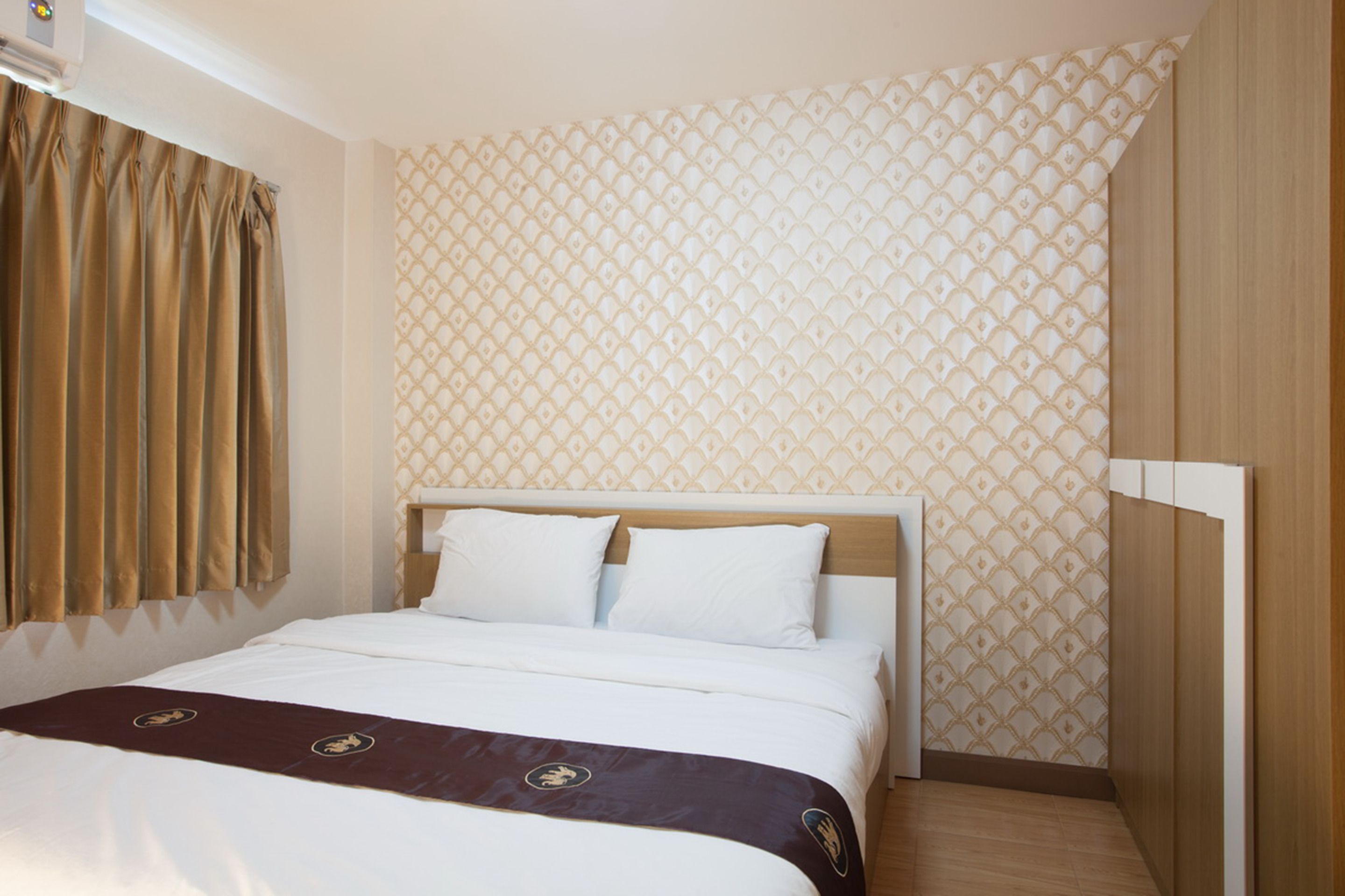 A hotel room with a bed, curtains, patterned wallpaper, and wooden flooring.