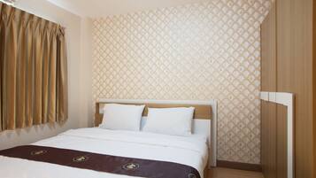 A hotel room with a bed, curtains, patterned wallpaper, and wooden flooring.