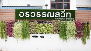 Letrero de Orawan Suites con una pared verde y plantas colgantes.