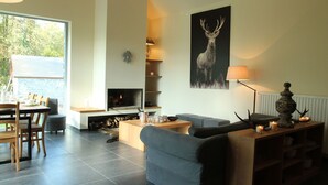 Una sala de estar moderna con chimenea, un comedor con mesa y sillas, y un cuadro grande de un ciervo en la pared.