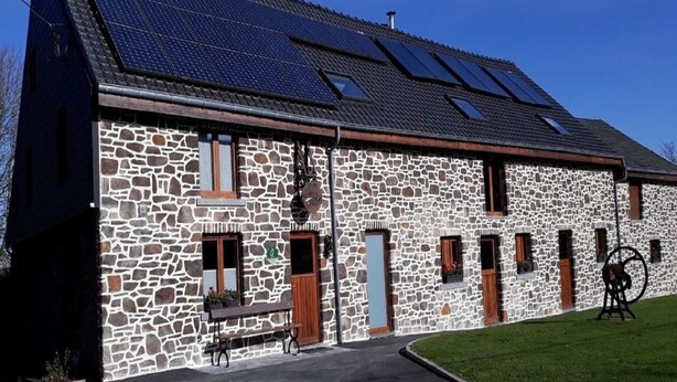 A stone building with a sloped roof, solar panels, and a bench outside.