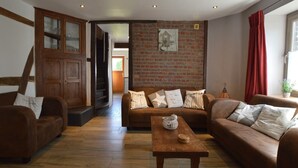 A cozy living room with a brick wall, wooden furniture, and a staircase leading to another room.
