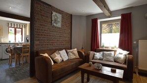 A cozy living room with a brown leather sofa, a wooden coffee table, and a brick wall.