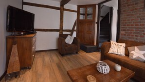 A cozy living room with exposed wooden beams, a television on a wooden cabinet, a sofa with cushions, and a coffee table with decorative items.