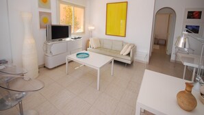 A modern living room with a sofa, a coffee table, a TV, and a large yellow artwork on the wall.