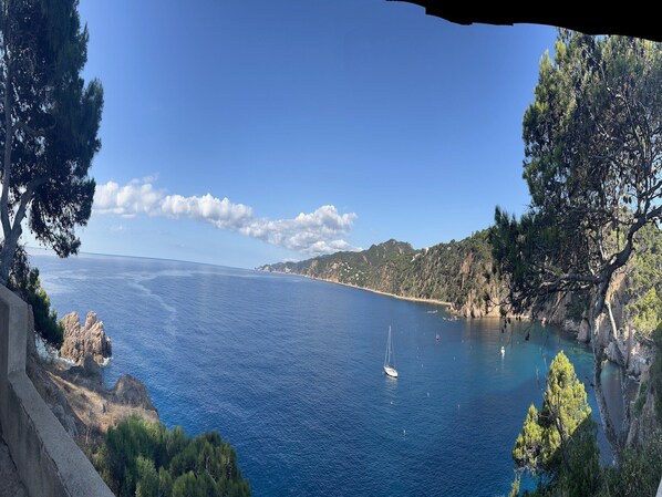 A coastal landscape with a clear view of the sea, a sailboat, and rocky cliffs.