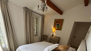 A bedroom with a bed, a round bedside table, a chair, a chandelier, and a door.