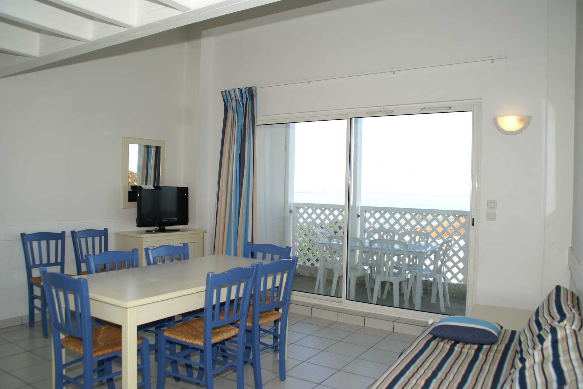 Un comedor con mesa y sillas, un televisor y un balcón con vistas.