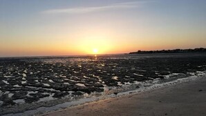 Ein Strand bei Sonnenuntergang, felsige Küstenlinie und eine ferne Küste mit Gebäuden.