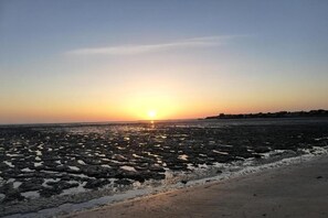Ein Strand bei Sonnenuntergang, felsige Küstenlinie und eine ferne Küste mit Gebäuden.