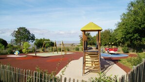 Ein Spielplatz mit einer hölzernen Kletterkonstruktion, Schaukeln und einem roten Spielbereich.