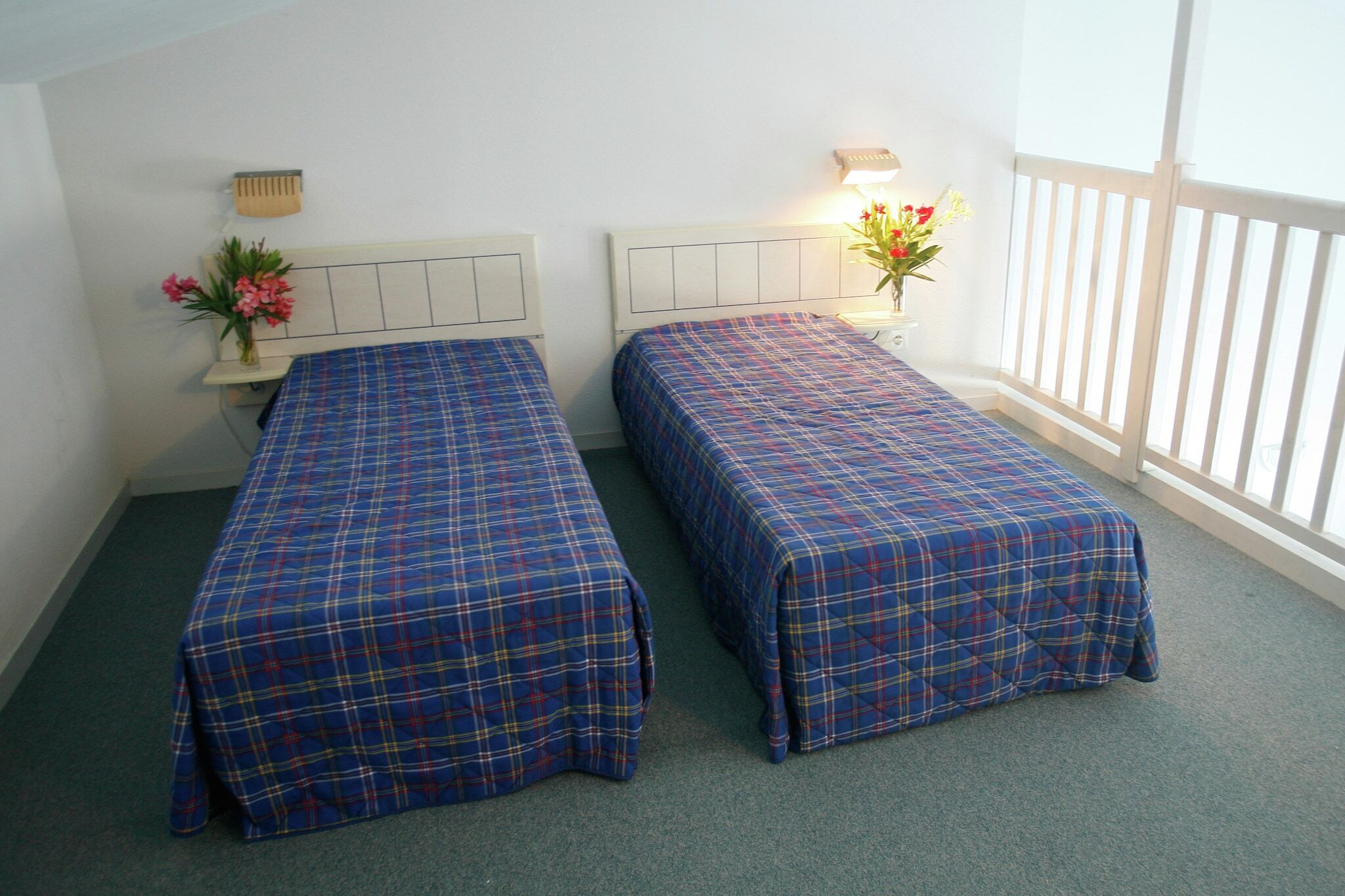 Una habitación con dos camas individuales, cada una con cabecera y mesita de noche con lámpara.