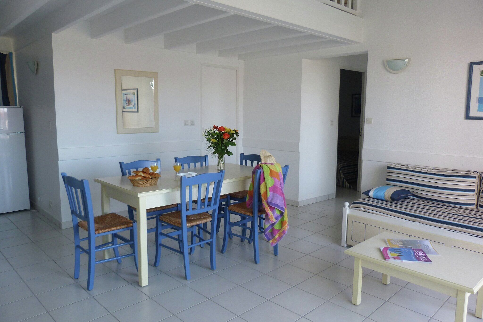 A dining area with a white table, blue chairs, and a vase with flowers.