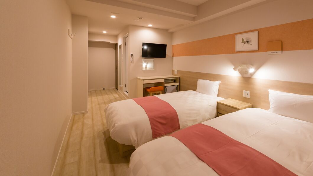 Habitació d'hotel amb dos llits, una taula de treball, televisió i petita cuina equipada.