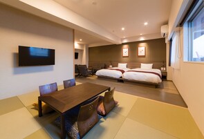 A hotel room with a wooden dining table, two beds, a TV, and a large window.