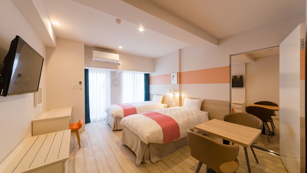 Habitació d'hotel amb dos llits, una taula, una cadira, un televisor i un mirall.