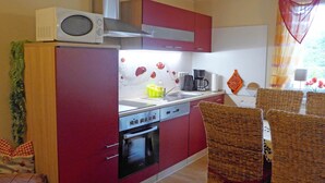 Una cucina compatta con mobili rossi, un forno a microonde, un fornello e una moka. C'è un'area pranzo con sedie in vimini e un tavolo.