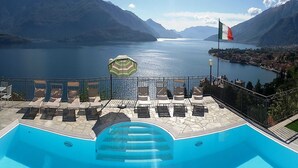Una piscina con sillas de descanso y una sombrilla, con vista a un lago y montañas al fondo.