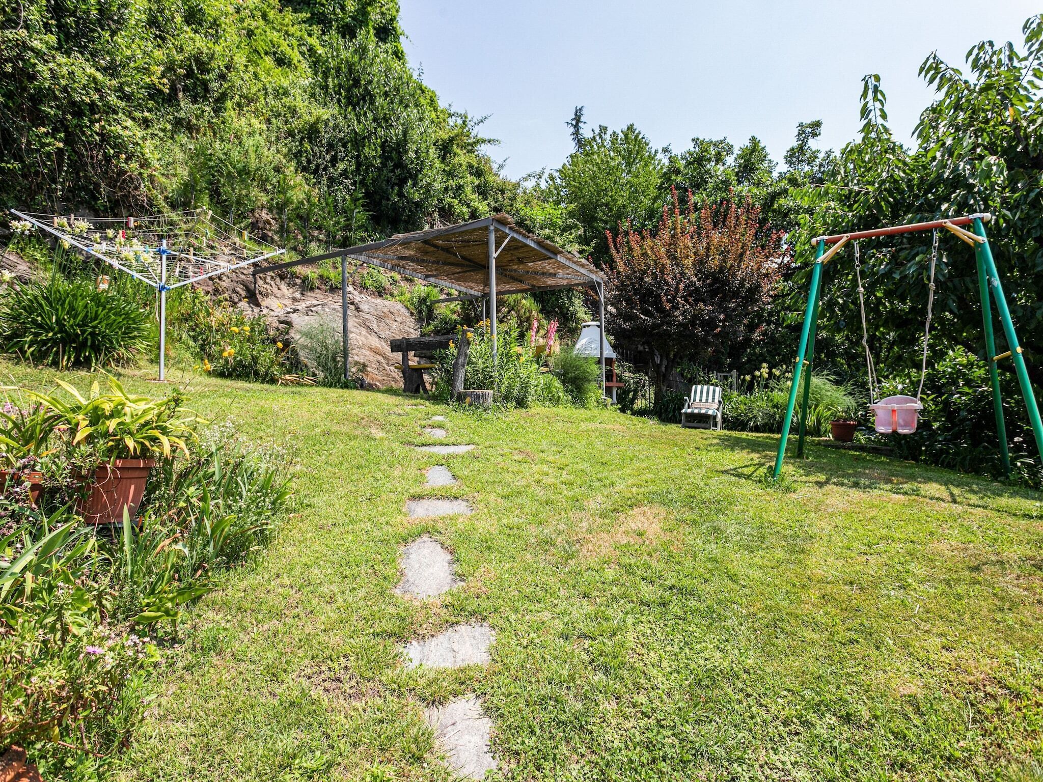 A garden with a swing set, a covered seating area, and a stone path.