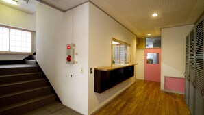 Un pasillo con piso de madera, una escalera, una recepción y una pared rosa.