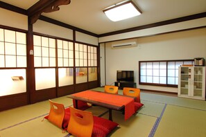 A traditional Japanese room with tatami flooring, a low table with a red tablecloth, orange chairs, and a television. - Guesthouse Fujinokura Kawaguchiko (Fujikawaguchiko)