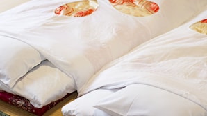 Una cama con ropa de cama blanca y una almohada roja.