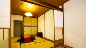 Una habitación japonesa tradicional con suelo de tatami, una mesa baja con cojín y puertas correderas.