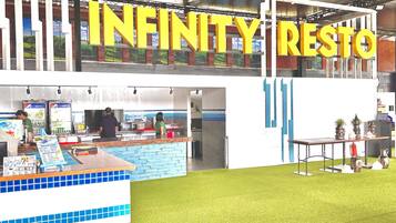 En restauranginteriör med en skylt som visar texten ”INFINITY RESTO” och en bardisk med blå kakelplattor på väggen bakom och ett ställ med menyer.