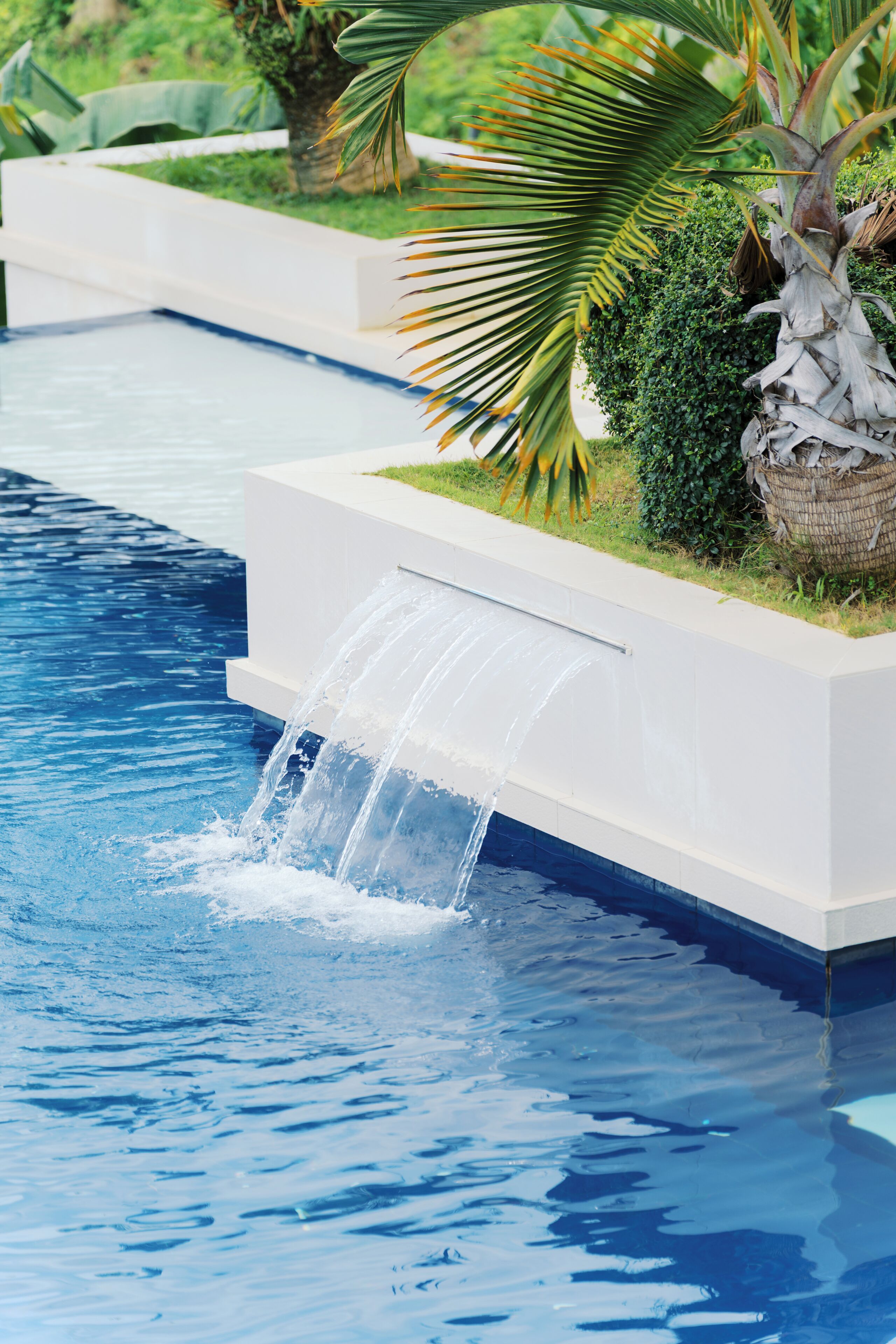 A swimming pool with a waterfall feature and surrounding greenery.