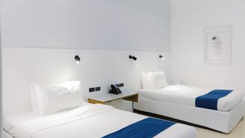 A hotel room with two beds, a bedside table with a phone, and a wall-mounted light fixture.