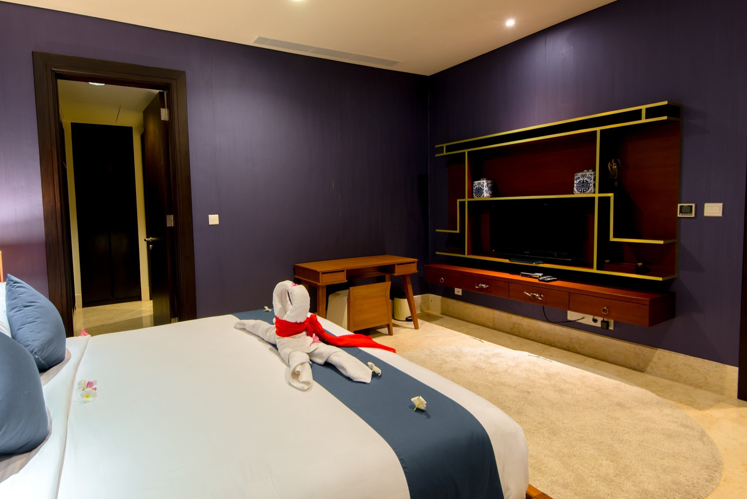 Habitación de hotel con una cama grande, un escritorio, un televisor montado en la pared y una puerta que da a otra habitación.