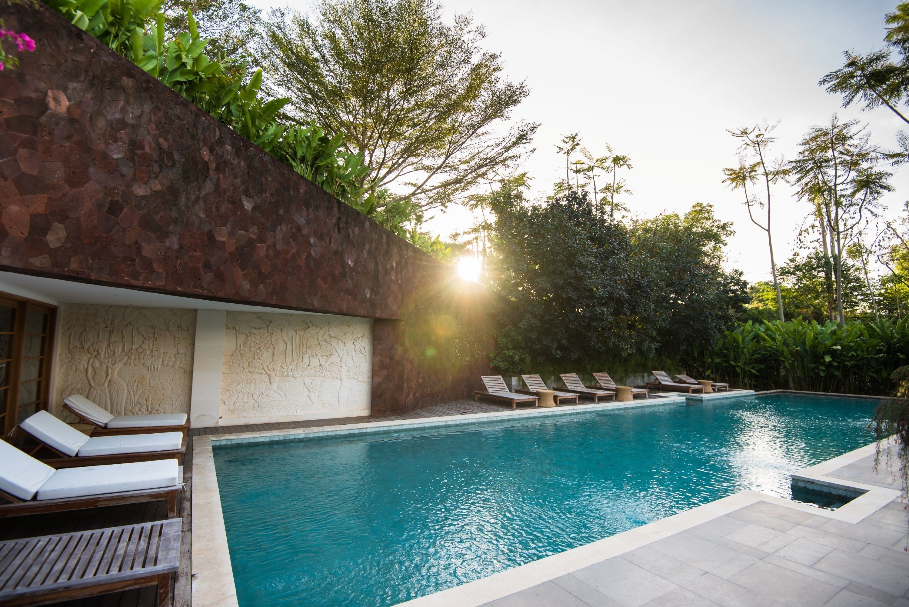 A swimming pool with lounge chairs and a stone wall.