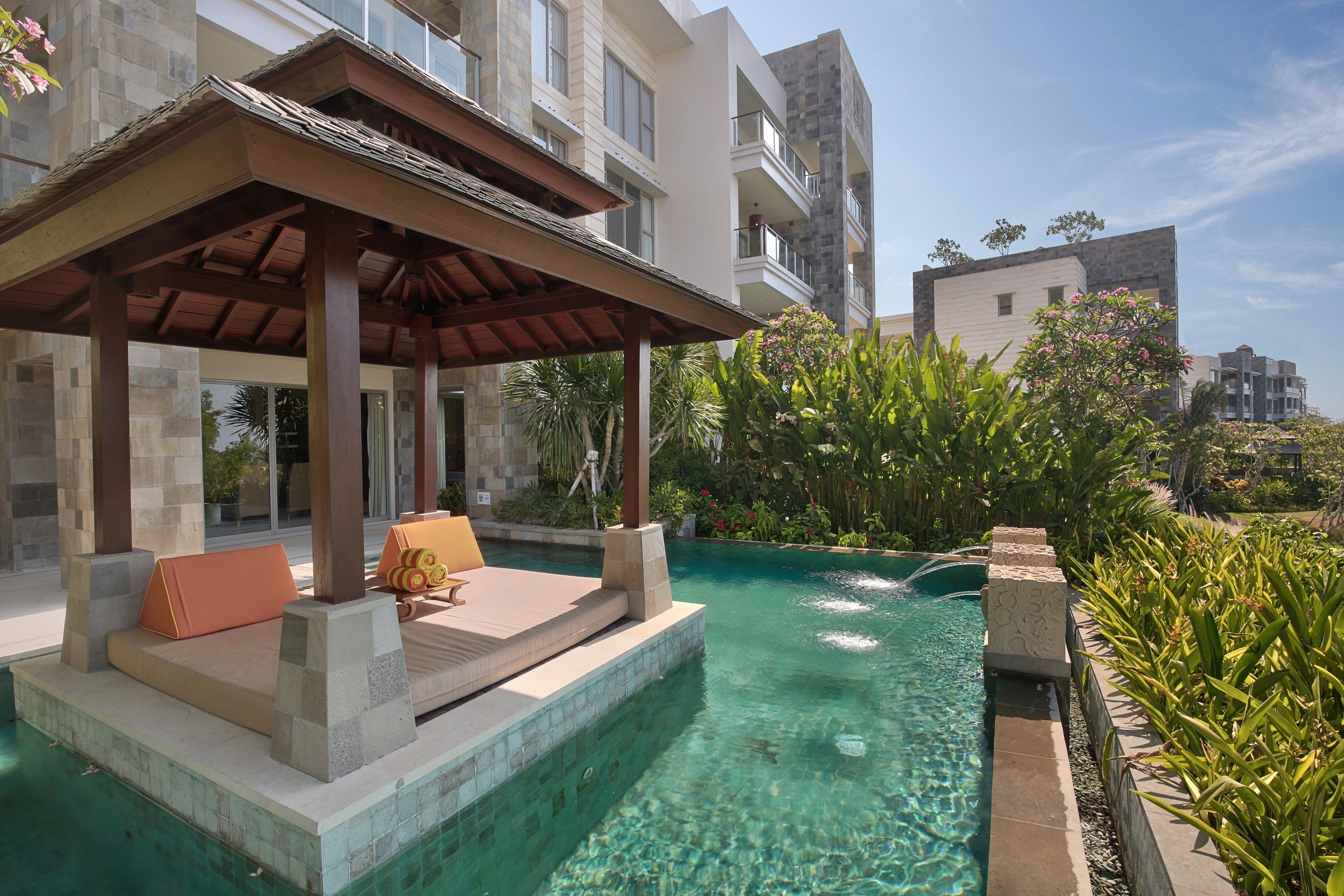 A pool area with a covered seating area, clear water, and surrounding greenery.